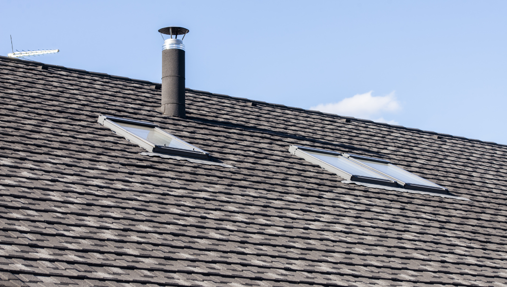 Close-up of a metal chimney vent and two skylights on an asphalt shingle roof.